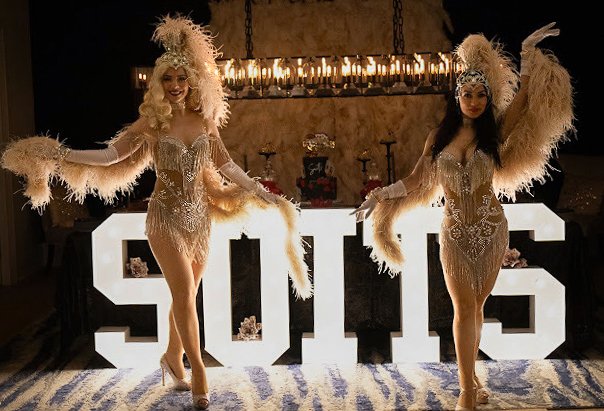 Showgirls in feathered costumes beside marquee letters